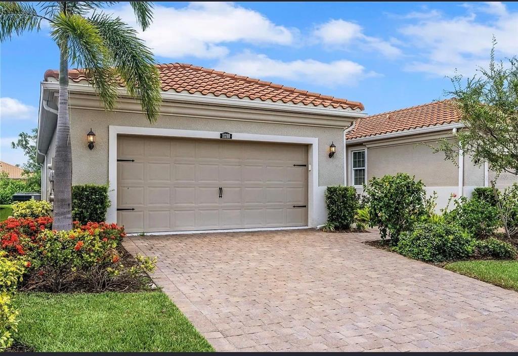 A beige house exterior features a two-car garage, a paved driveway, and a palm tree — 11780 TAPESTRY LANE, VENICE, FL