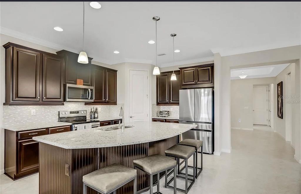 A kitchen with dark wood cabinets, granite countertops, a large island, and stainless steel appliances — 11780 TAPESTRY LANE, VENICE, FL