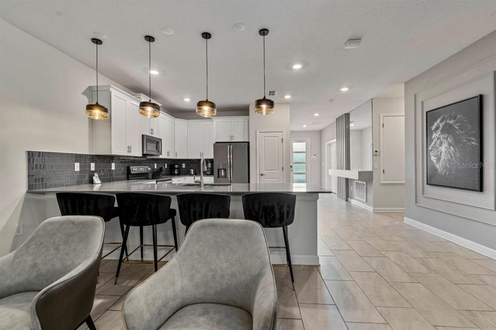 A modern kitchen features white cabinetry, a gray tile backsplash, and four pendant lights — 2830 STOREY COVE AVENUE, KISSIMMEE, FL