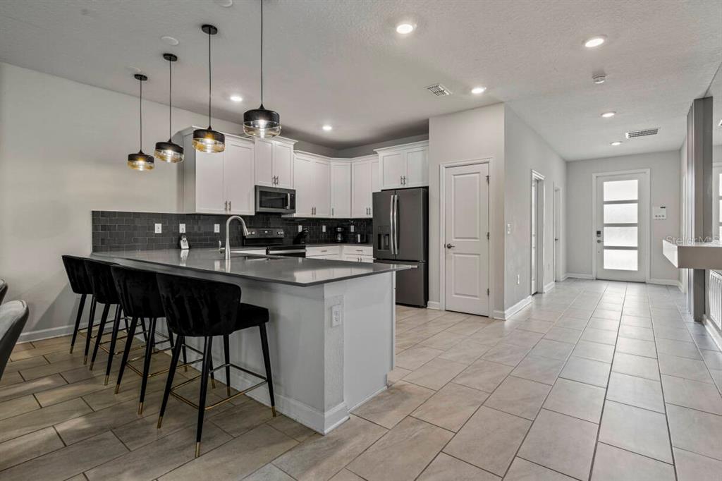 A modern kitchen features a gray island with bar stools, white cabinetry, and tile flooring — 2830 STOREY COVE AVENUE, KISSIMMEE, FL