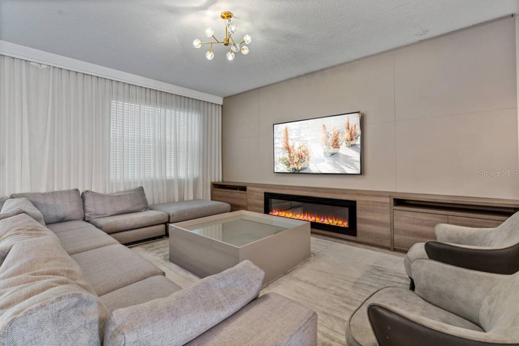 A modern living room features a large sectional sofa, fireplace, wall-mounted television, and chandelier — 2830 STOREY COVE AVENUE, KISSIMMEE, FL
