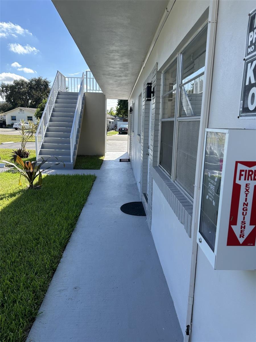 A concrete walkway leads past a white building with an exterior staircase and fire extinguisher — 6101 Garfield St, Hollywood FL 33024, HOLLYWOOD, FL