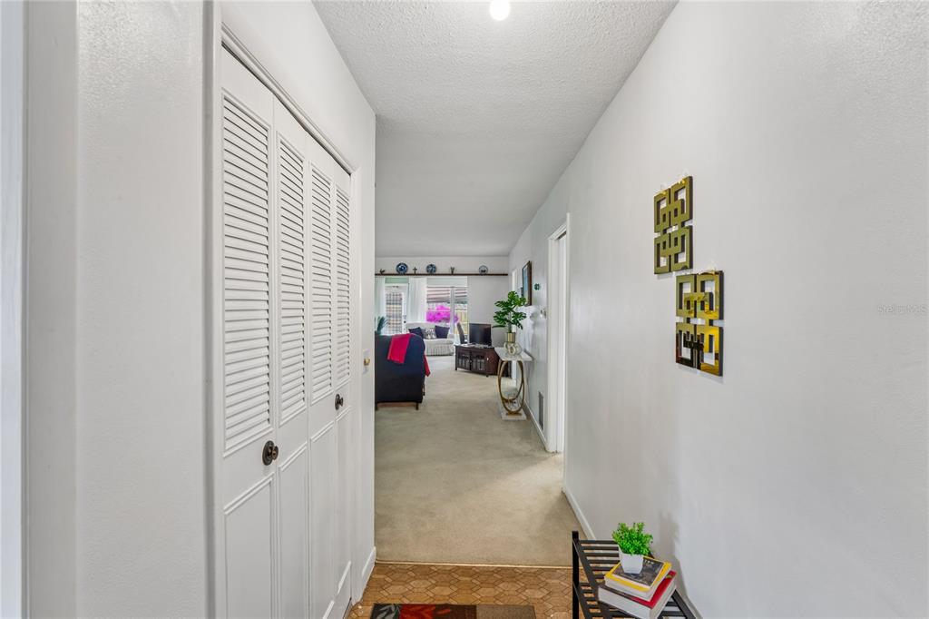 A hallway with white walls, a louvered closet door, and a view into a living room — 1611 S LAKE AVENUE UNIT 1, CLEARWATER, FL