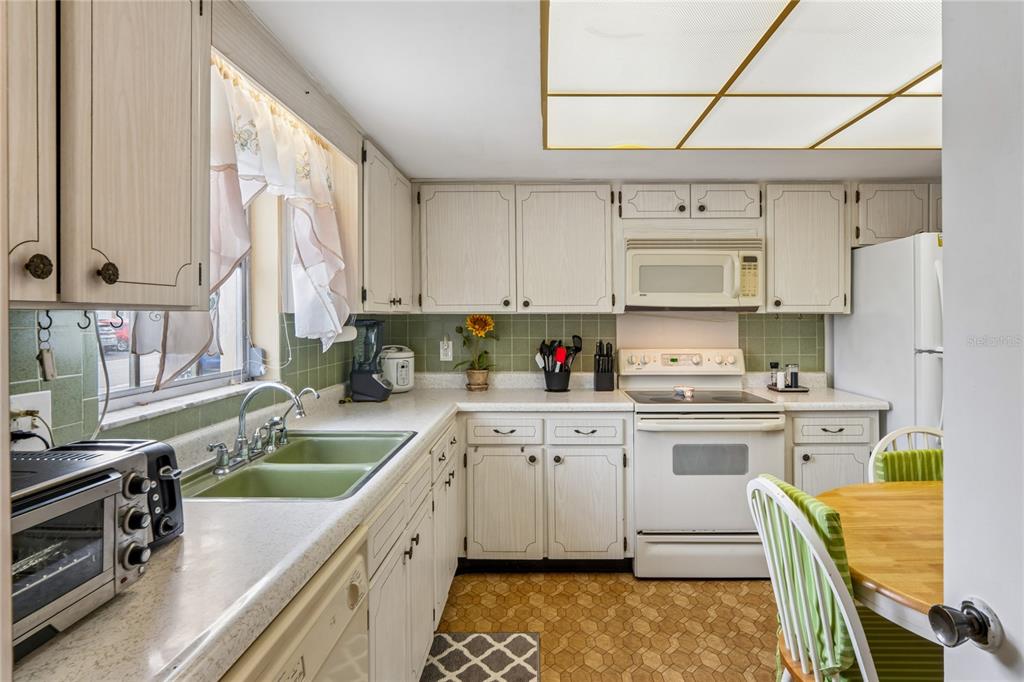A kitchen features white cabinets, green tile backsplash, a double sink, and a dining area — 1611 S LAKE AVENUE UNIT 1, CLEARWATER, FL