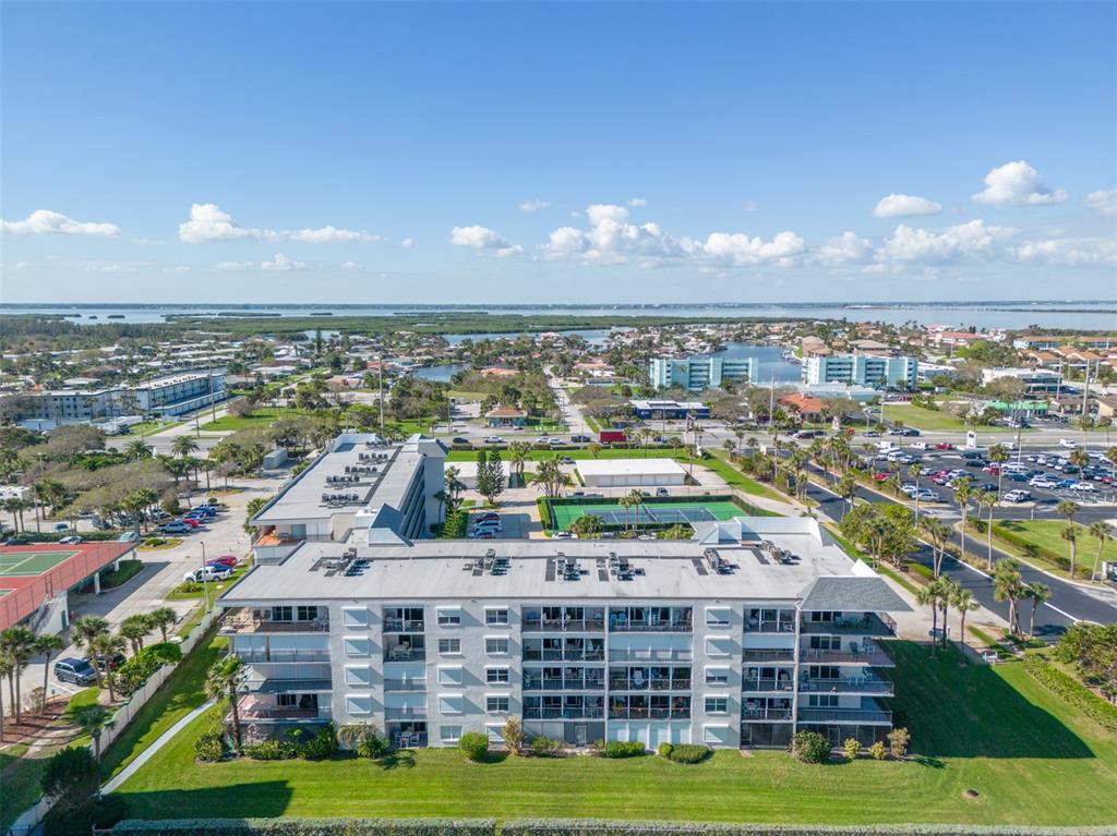 An aerial view shows a multi-story apartment building with balconies, a tennis court, and parking — 1700 N ATLANTIC AVENUE UNIT 126, COCOA BEACH, FL