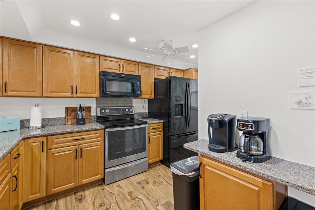 A kitchen features wood cabinets, granite countertops, stainless steel appliances, and a black refrigerator — 1700 N ATLANTIC AVENUE UNIT 126, COCOA BEACH, FL