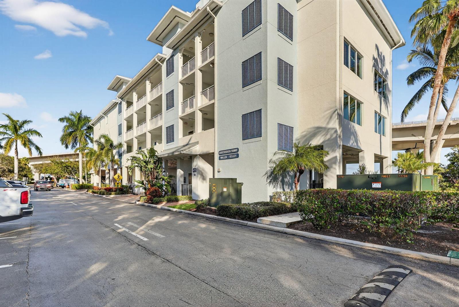 A multi-story apartment building with balconies and palm trees stands beside a paved parking area — 415 NW Flagler Avenue # 403, Stuart FL 34994, STUART, FL