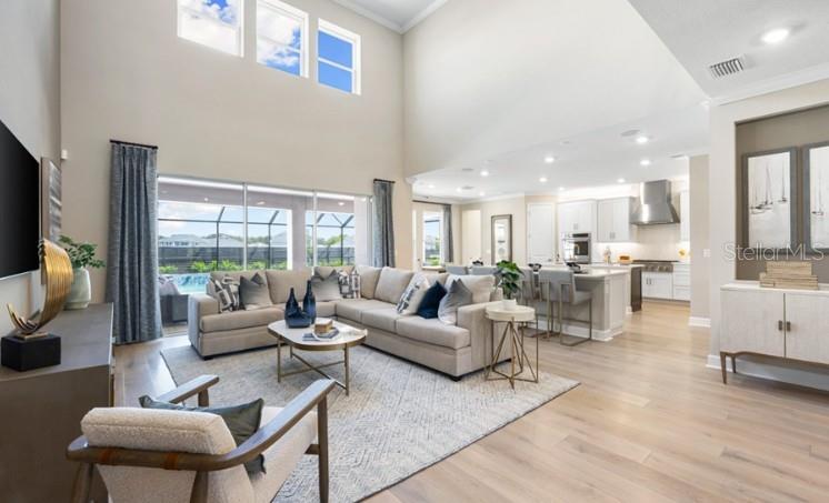 A bright, open-concept living room with high ceilings, light wood floors, and a modern kitchen — 11270 KINGLY LANE, ODESSA, FL