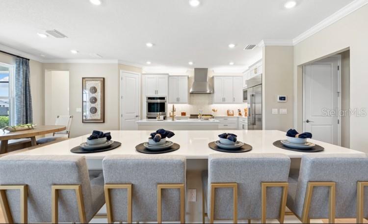 A modern kitchen features white cabinetry, a large island with four chairs, and stainless appliances — 11270 KINGLY LANE, ODESSA, FL