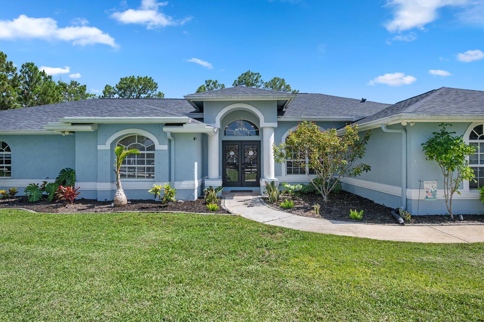 A light blue single-story house with a dark roof and a central arched entryway — 14862 85th Road N, FL 33470, FL