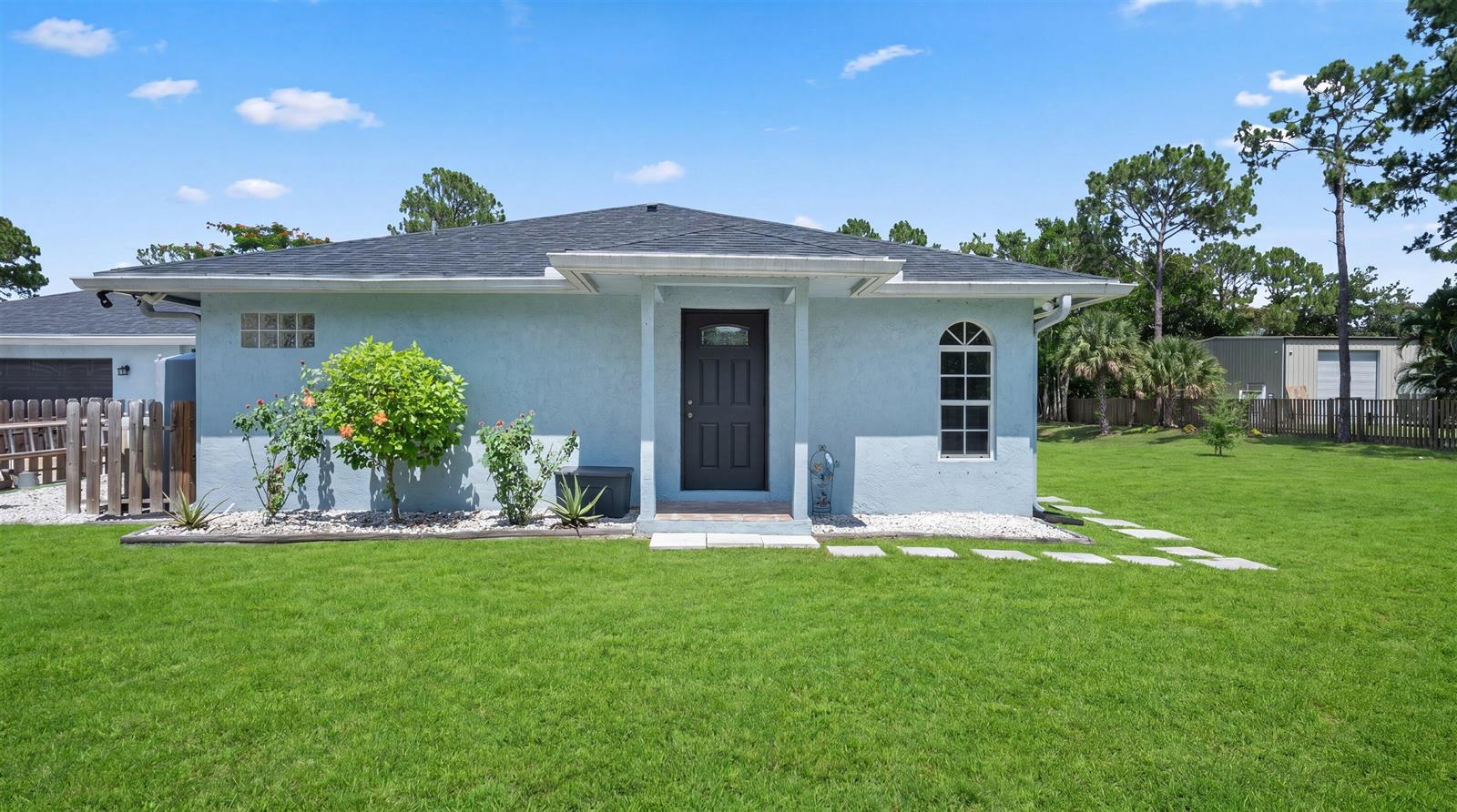 A light blue single-story house with a dark front door and a large green lawn — 14862 85th Road N, FL 33470, FL
