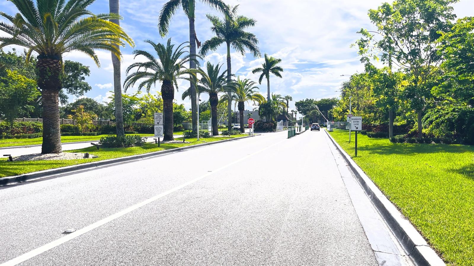 A paved road leads toward a gated community entrance lined with palm trees and grass — 15640 Bottlebrush Circle, Delray Beach FL 33484, DELRAY BEACH, FL