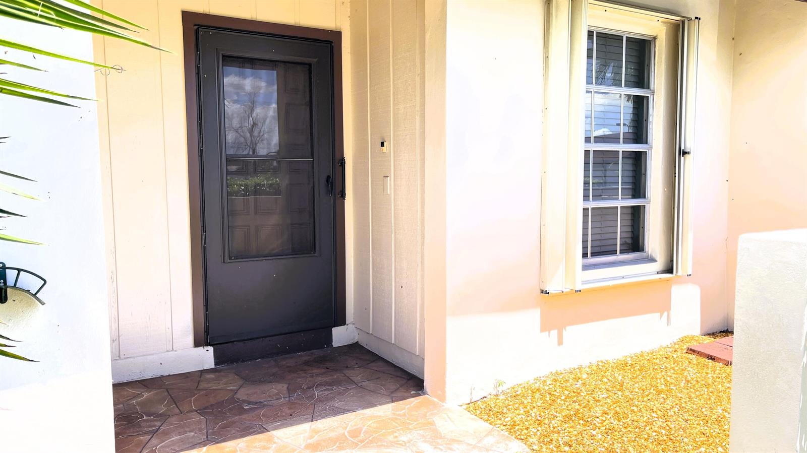 A front entryway features a dark storm door, a window with shutters, and stone flooring — 15640 Bottlebrush Circle, Delray Beach FL 33484, DELRAY BEACH, FL