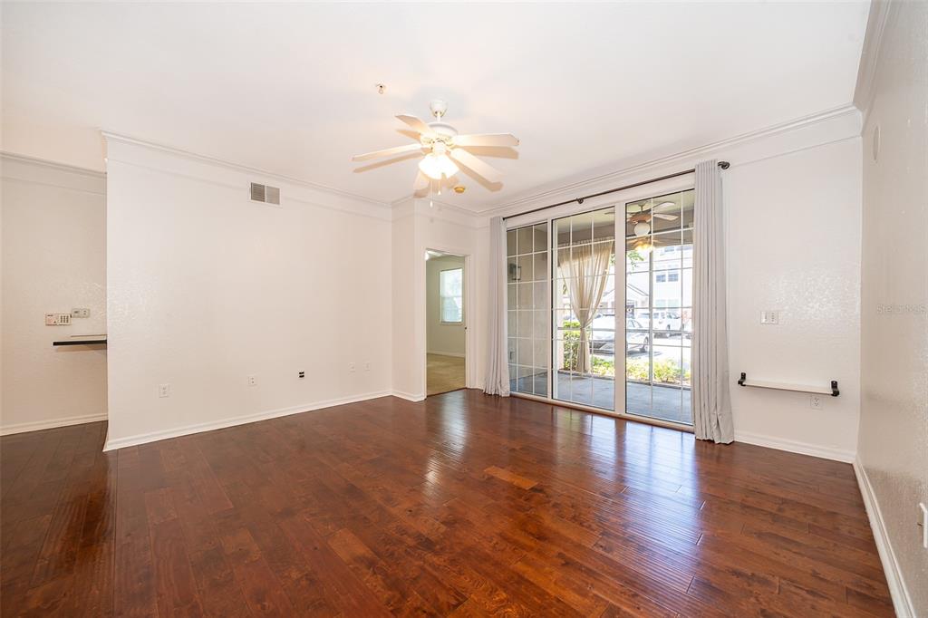 An empty living room features dark hardwood floors, a ceiling fan, and sliding glass doors — 6663 QUEENS BOROUGH AVENUE UNIT 101, ORLANDO, FL