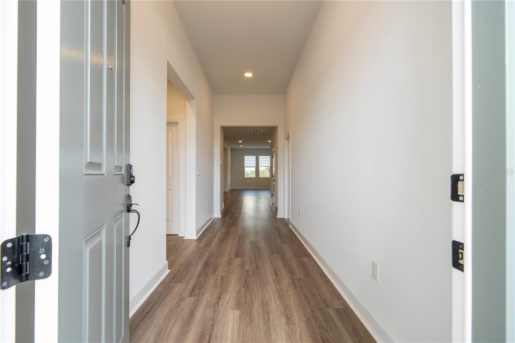 A view from an open front door into a hallway with light wood-look flooring — 734 CREEPING FIG STREET, APOPKA, FL