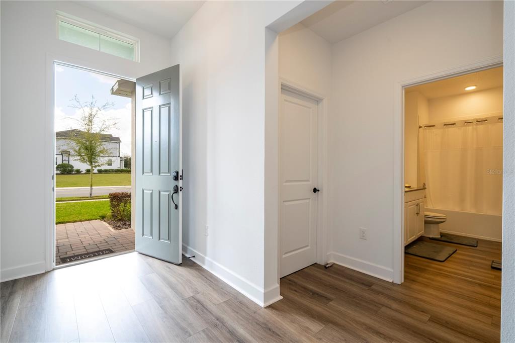 An entryway with wood-look flooring, a light blue front door, and an adjacent bathroom — 734 CREEPING FIG STREET, APOPKA, FL