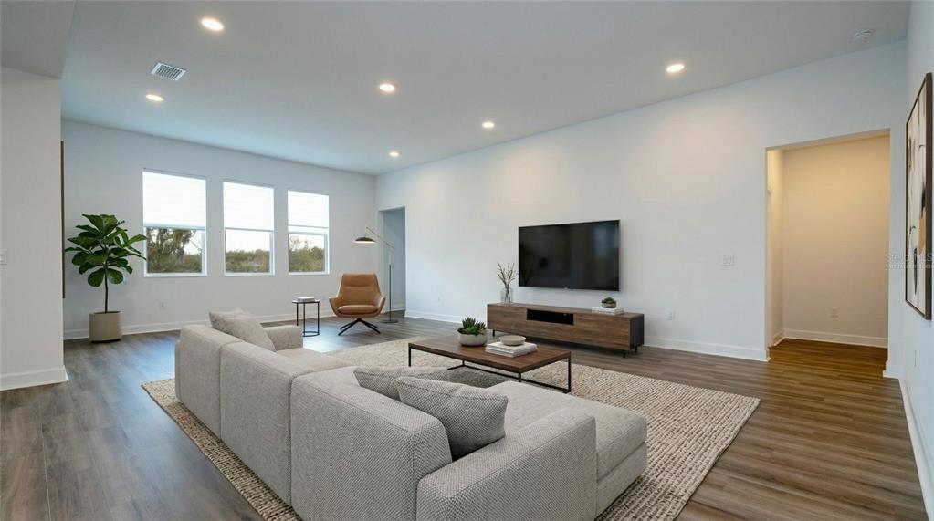 A modern living room features a light gray sectional sofa, a television, and wood flooring — 734 CREEPING FIG STREET, APOPKA, FL