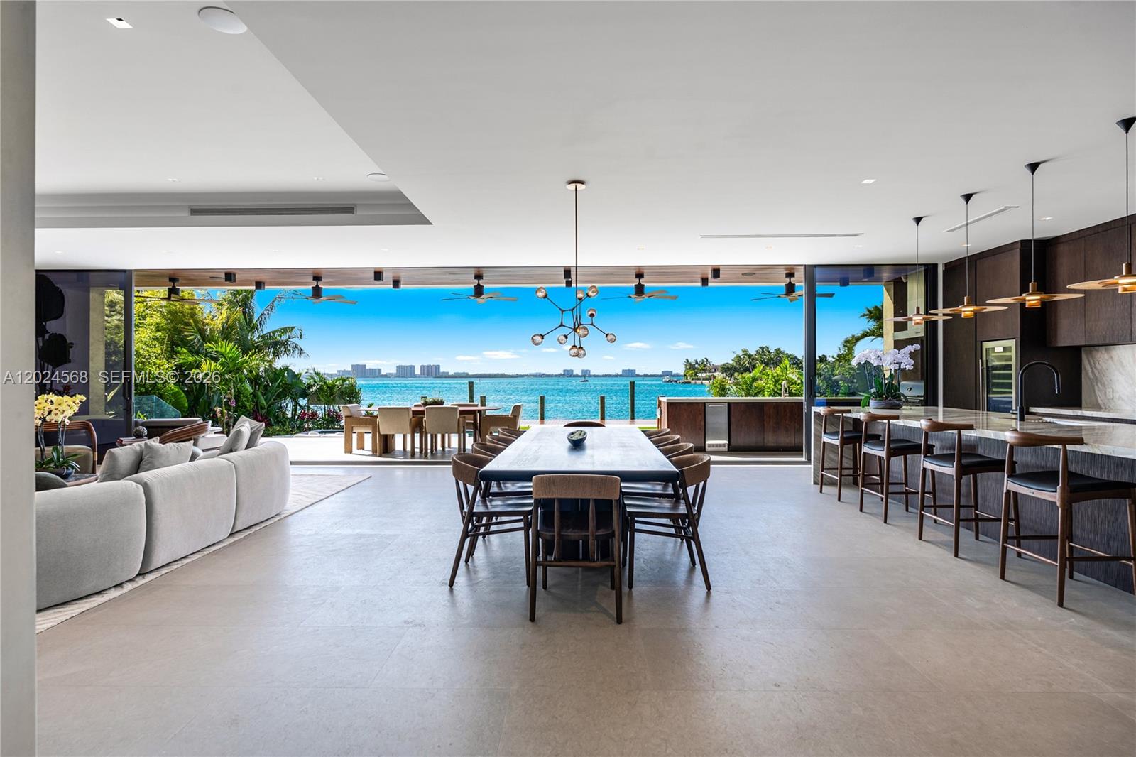 An open-concept living and dining area features floor-to-ceiling glass doors overlooking a waterfront view — 857 N Shore Dr, Miami Beach FL 33141, MIAMI BEACH, FL