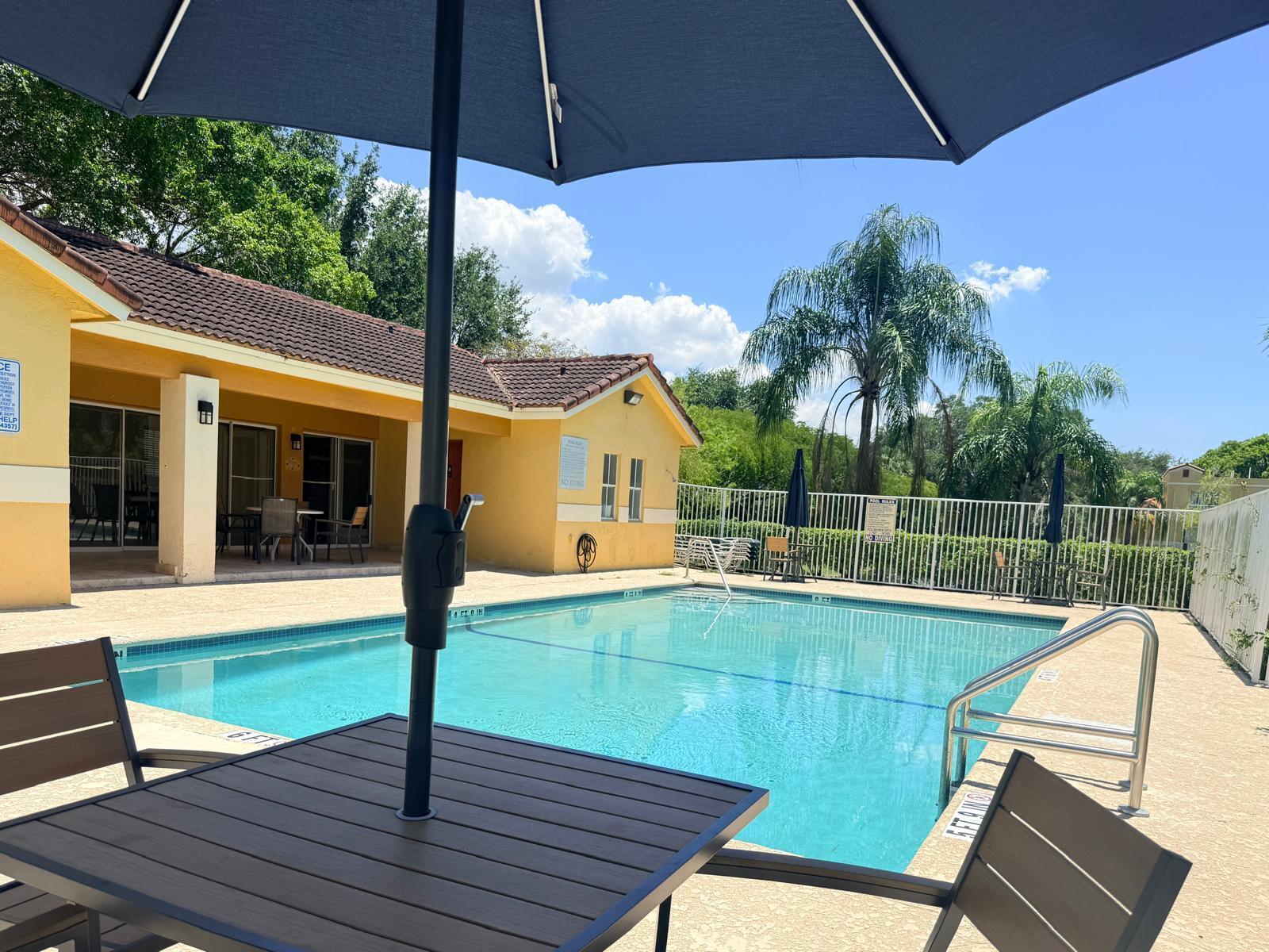 A swimming pool with a patio, outdoor furniture, and a yellow building under a blue sky — 3832 NW 90th Avenue # 3832, Sunrise FL 33351, SUNRISE, FL
