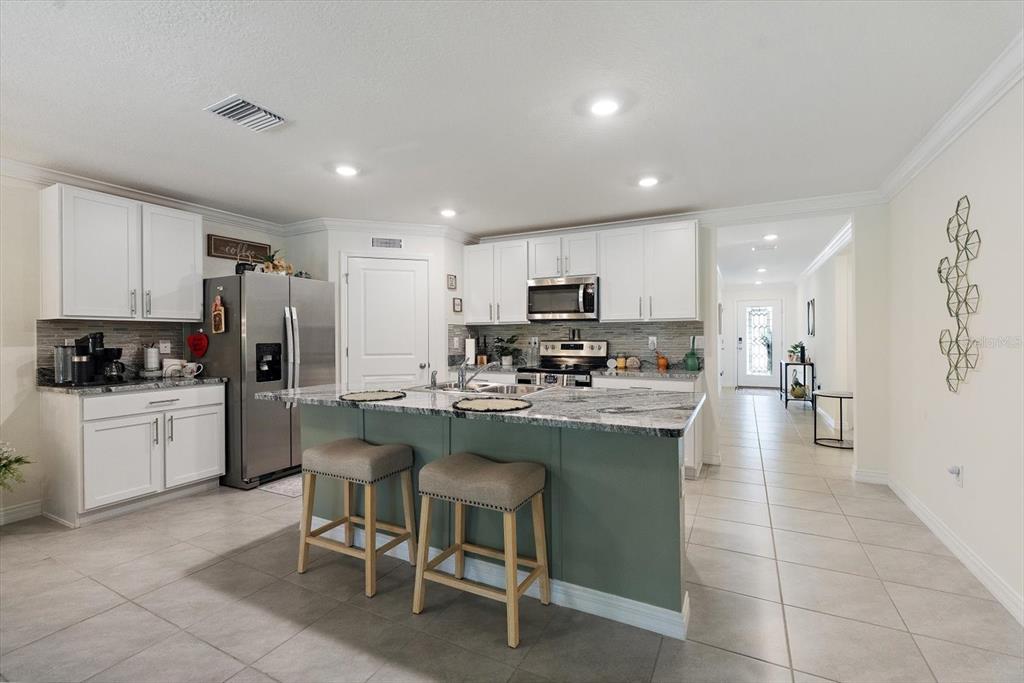 A kitchen features white cabinets, a green island with bar stools, and stainless steel appliances — 5223 BYRONIC COURT, BROOKSVILLE, FL