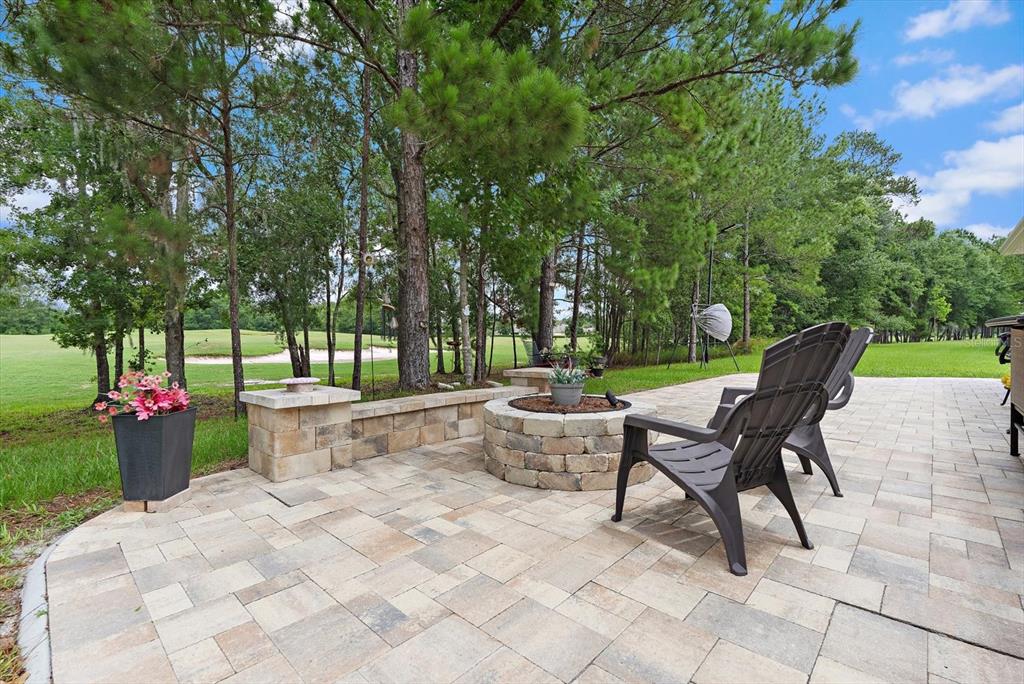 A stone fire pit and patio chairs sit on a paved patio overlooking a golf course — 5223 BYRONIC COURT, BROOKSVILLE, FL