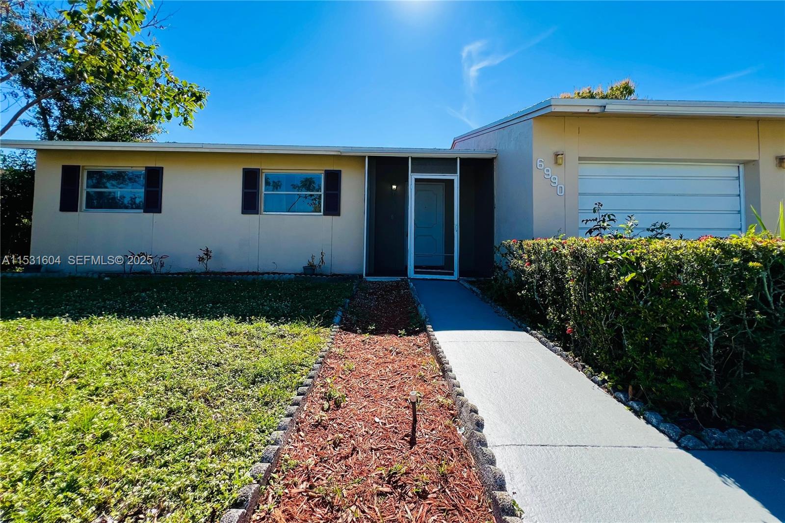 A single-story house features a light-colored exterior, a concrete walkway, and an attached garage — 6990 SW 1st St, Margate FL 33068, MARGATE, FL