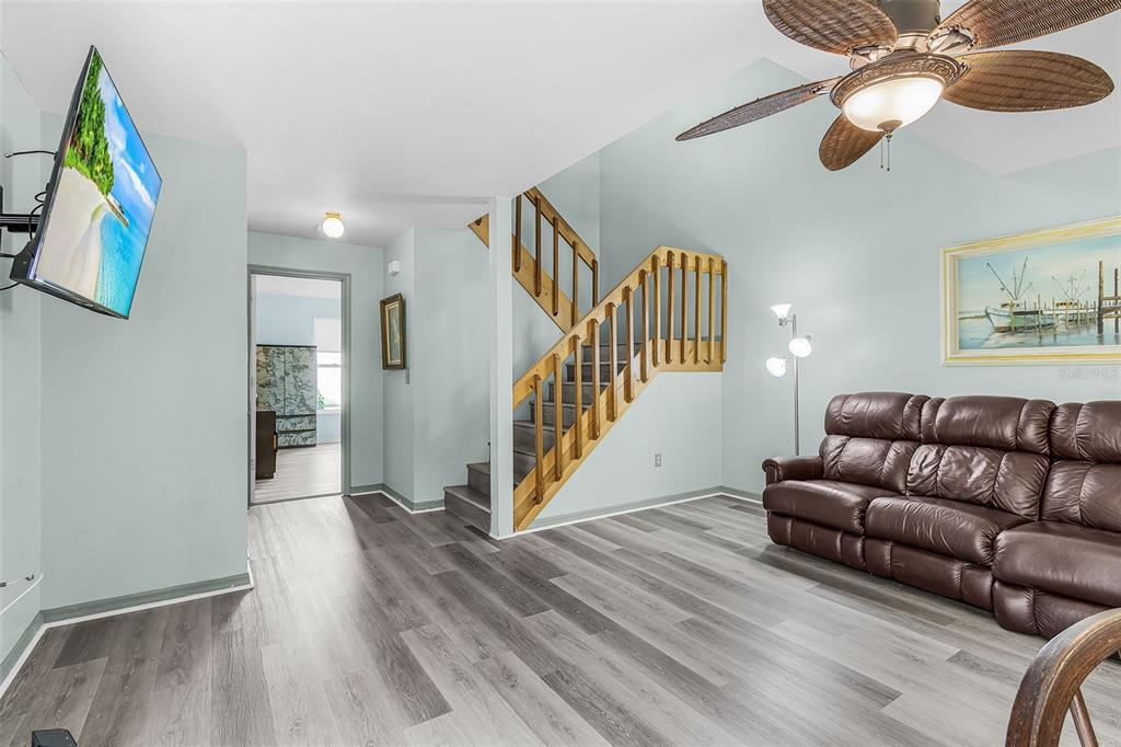 A living room features wood-look flooring, a brown leather sofa, and a wooden staircase — 13721 MARKHAM LANE UNIT 4, FORT MYERS, FL