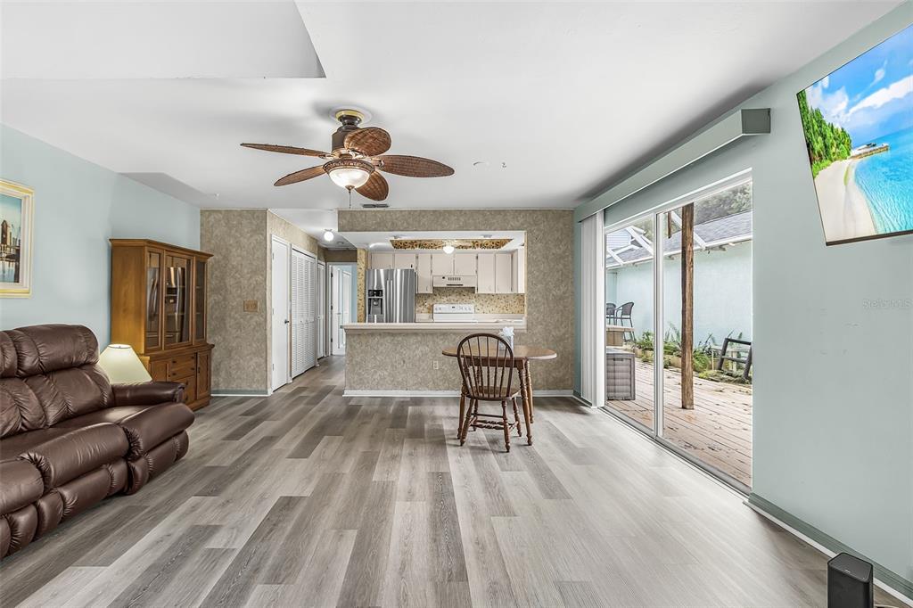 A living room with wood-look flooring, a ceiling fan, and a view into the kitchen — 13721 MARKHAM LANE UNIT 4, FORT MYERS, FL