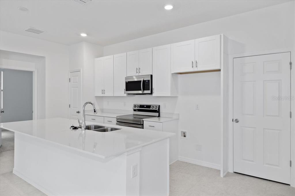 A modern kitchen features white cabinets, stainless steel appliances, and a large quartz island — 1194 ATLANTIC AVENUE, FRUITLAND PARK, FL