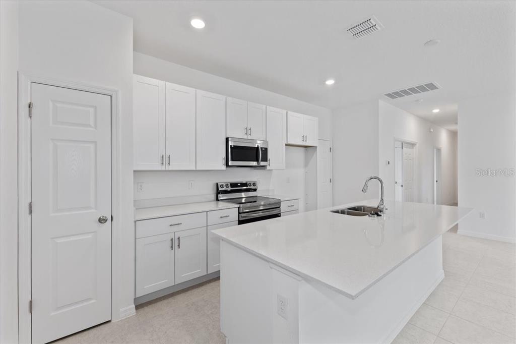 A modern kitchen features white cabinets, stainless steel appliances, and a large quartz-topped island — 1194 ATLANTIC AVENUE, FRUITLAND PARK, FL