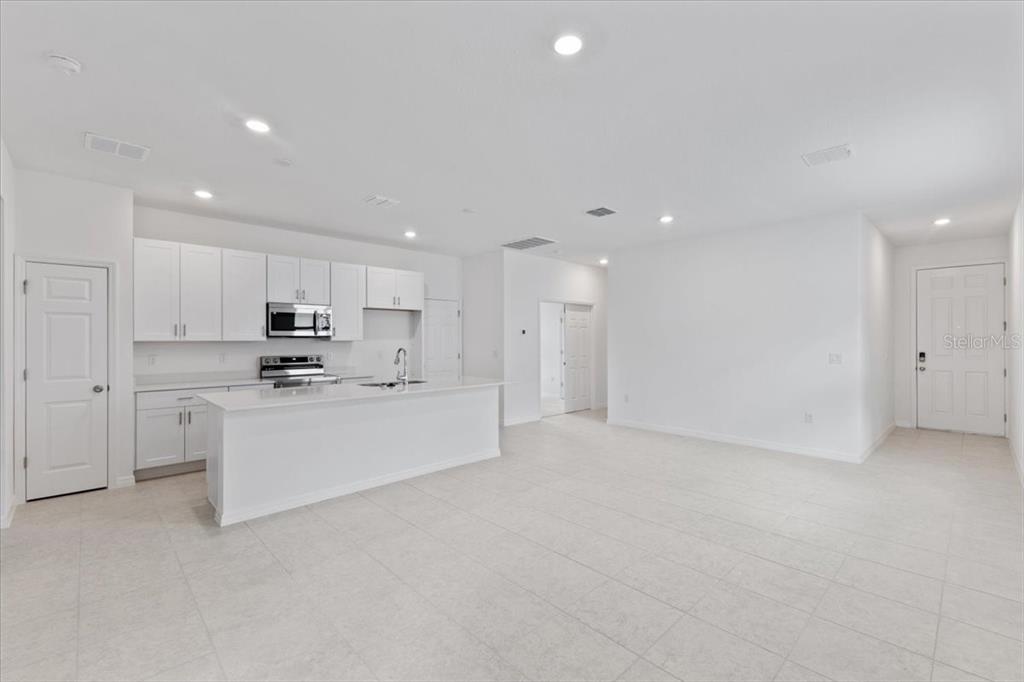 A bright, open-concept kitchen features white cabinetry, stainless steel appliances, and light tile flooring — 1194 ATLANTIC AVENUE, FRUITLAND PARK, FL
