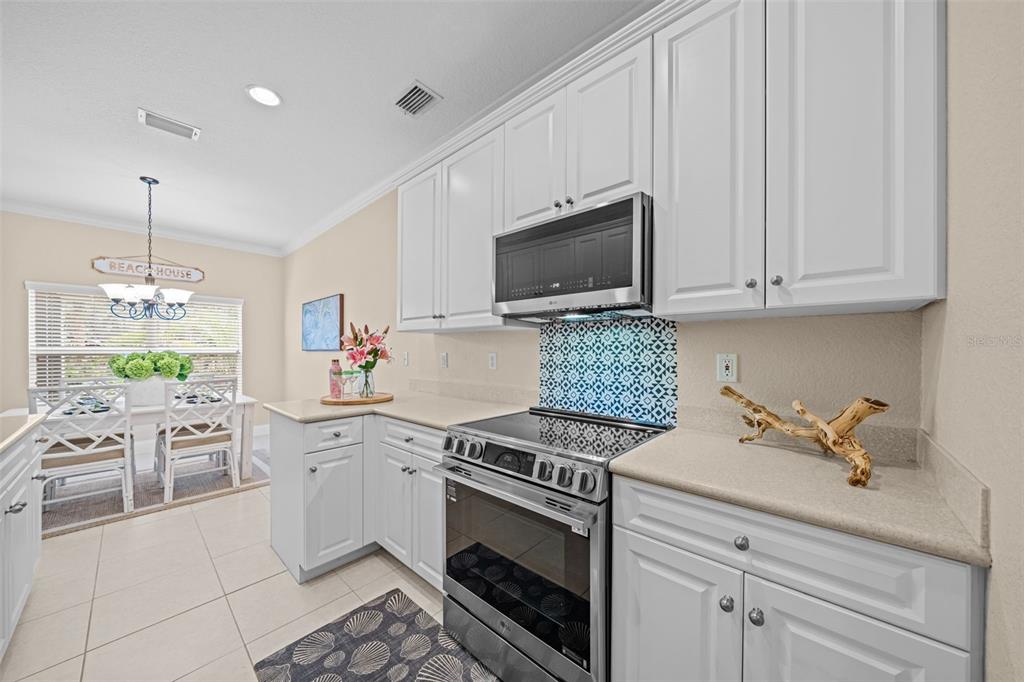 A white kitchen features a stainless steel range, patterned backsplash, and an adjacent dining area — 202 KING NEPTUNE LANE UNIT 202, CAPE CANAVERAL, FL