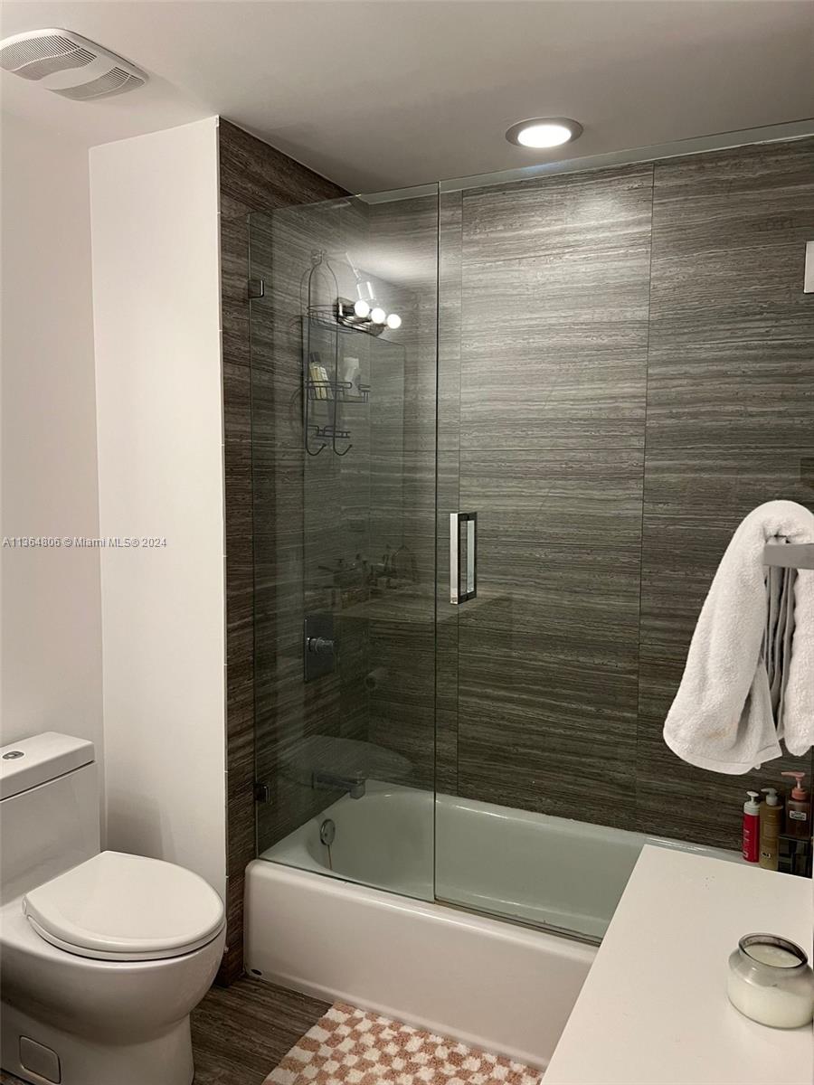 A bathroom features a white toilet, a bathtub with a glass door, and wood-patterned tiles — 1010 Brickell Ave # 2010, Miami FL 33131, MIAMI, FL