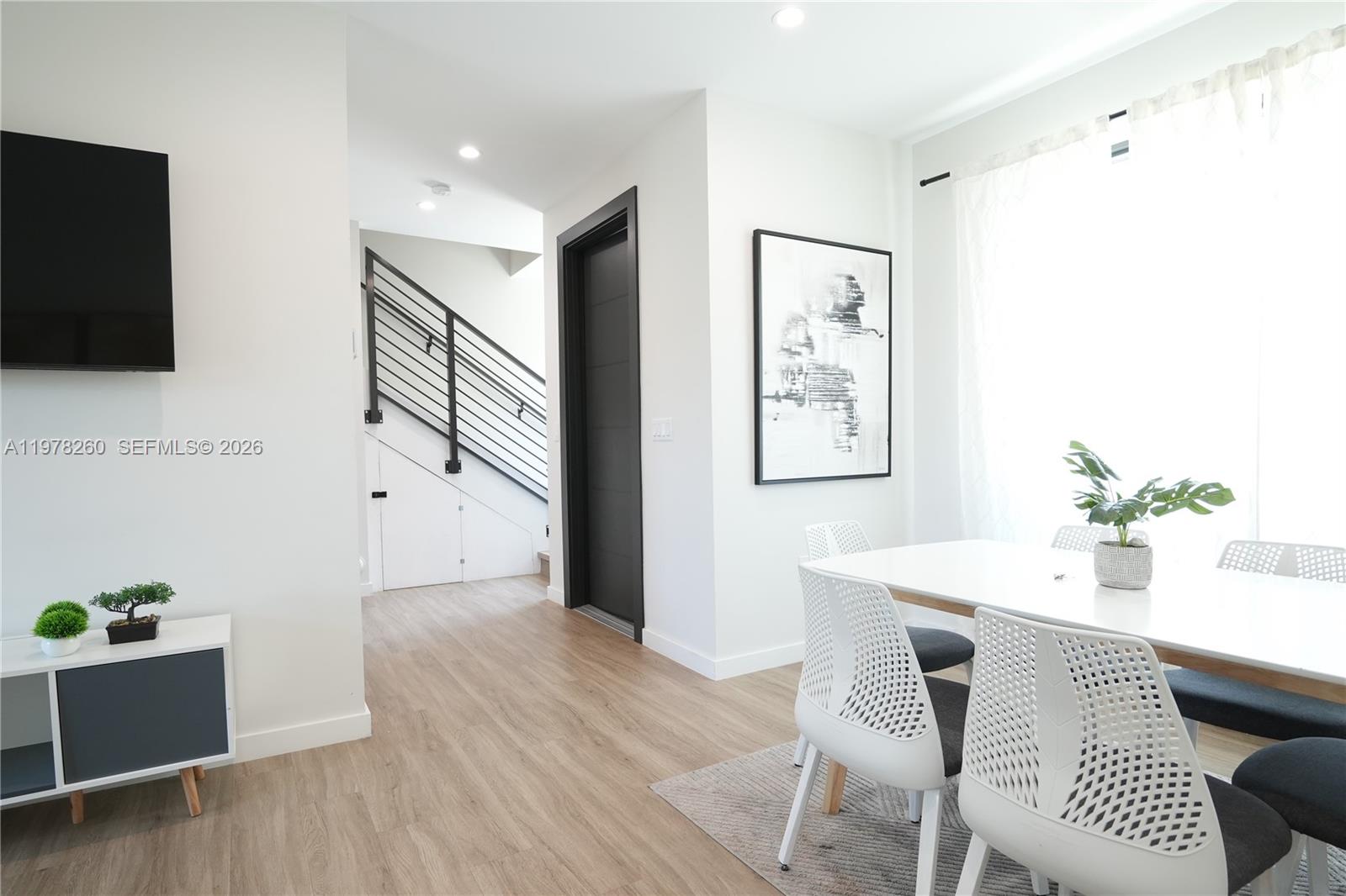 A modern dining area features white chairs, a table, and a staircase with black railings — 211 SE 4th St # 3, Hallandale Beach FL 33009, HALLANDALE BEACH, FL