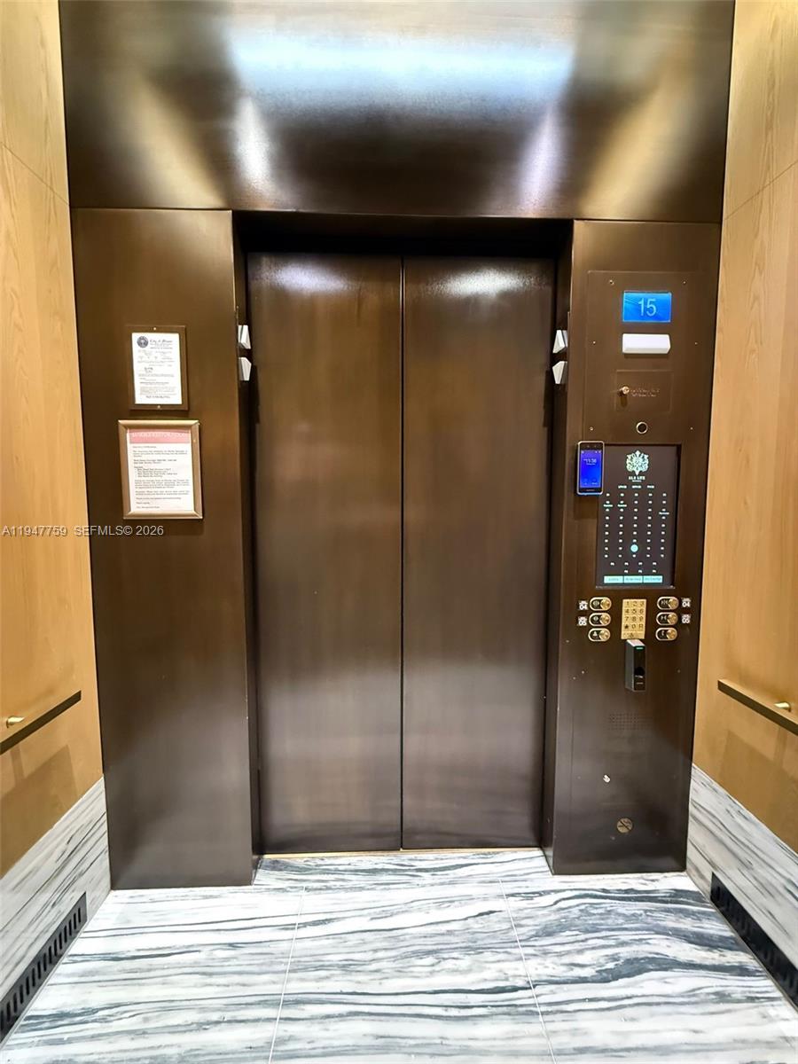 An elevator interior features dark metal doors, wood-paneled walls, and a marble floor — 801 S Miami Ave # 1804, Miami FL 33130, MIAMI, FL