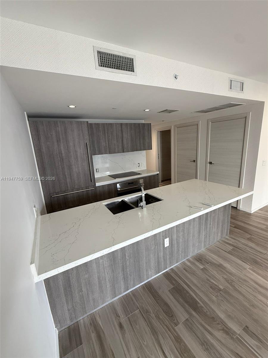 A modern kitchen features a white quartz island, gray wood-grain cabinetry, and stainless steel appliances — 801 S Miami Ave # 1804, Miami FL 33130, MIAMI, FL