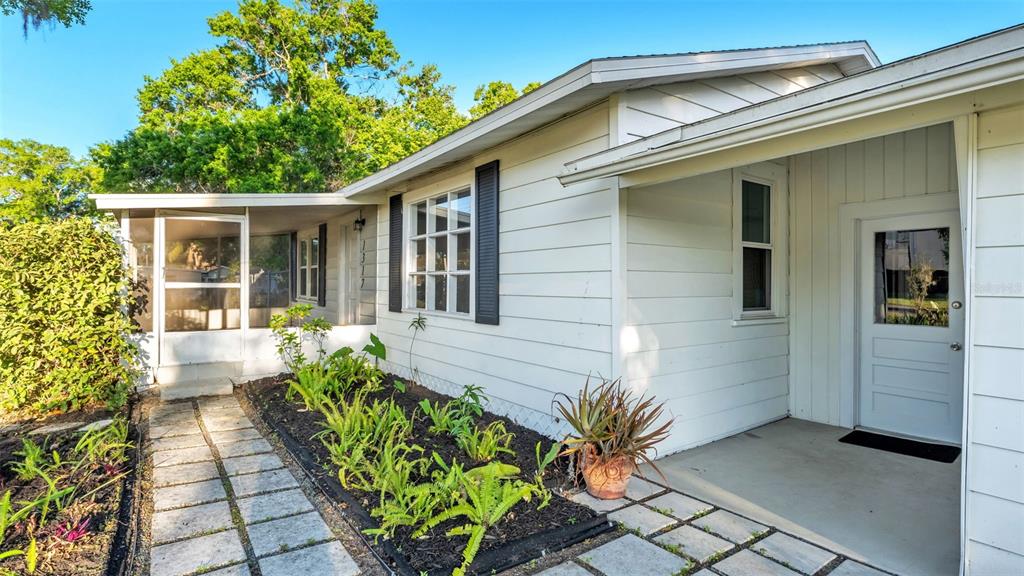 A white house exterior features a screened porch, a front door, and a stone walkway — 1317 W BELMAR STREET, LAKELAND, FL