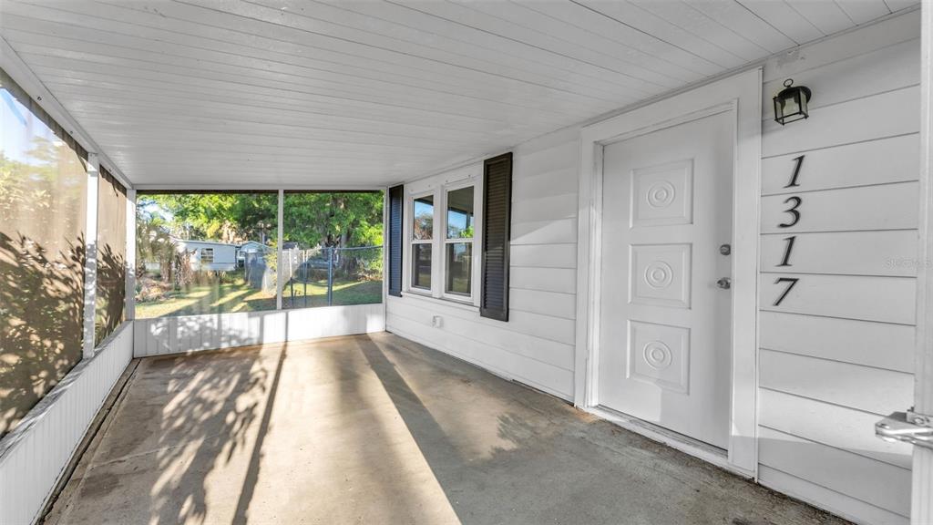 A white-walled covered porch features a screened enclosure, a concrete floor, and a front door — 1317 W BELMAR STREET, LAKELAND, FL