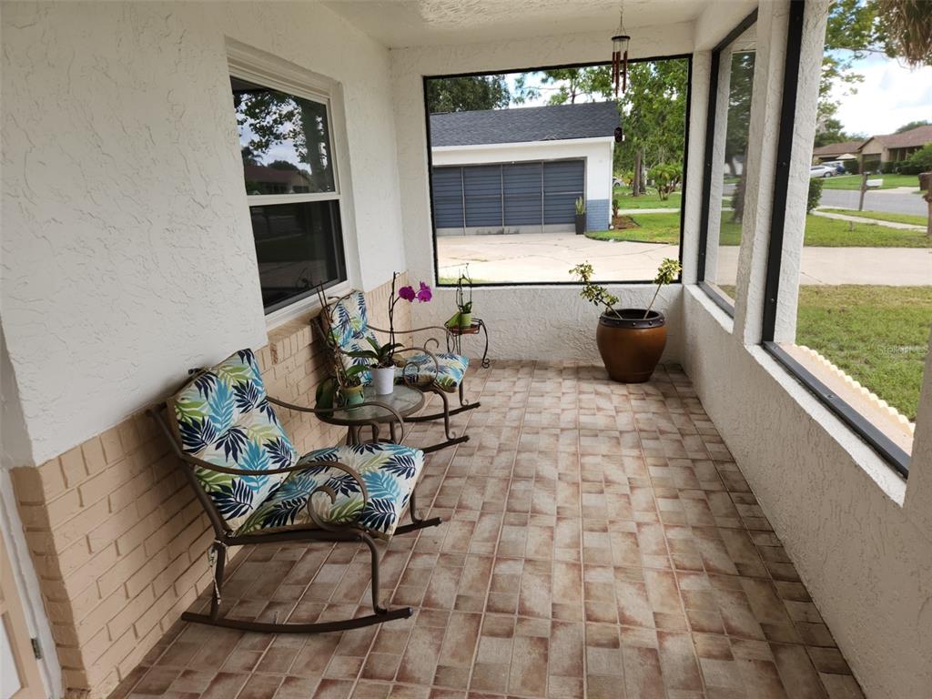 A screened-in porch features tiled flooring, two rocking chairs with patterned cushions, and exterior views — 2518 BOWMER DRIVE, KISSIMMEE, FL