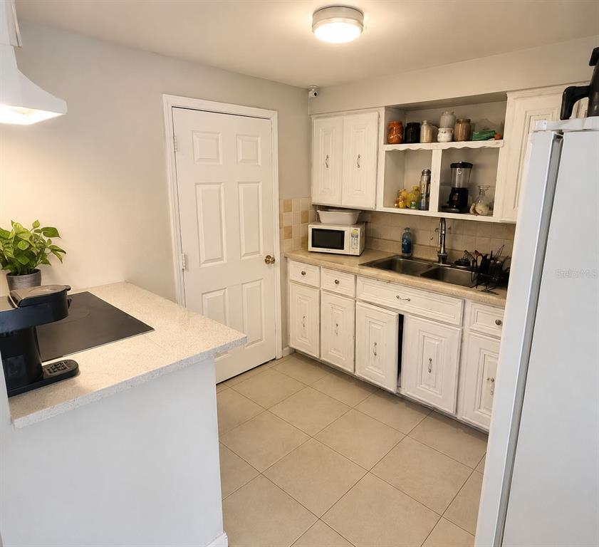 A kitchen features white cabinets, a double sink, a microwave, and light-colored tile flooring — 5801 BROOKGREEN AVENUE, ORLANDO, FL