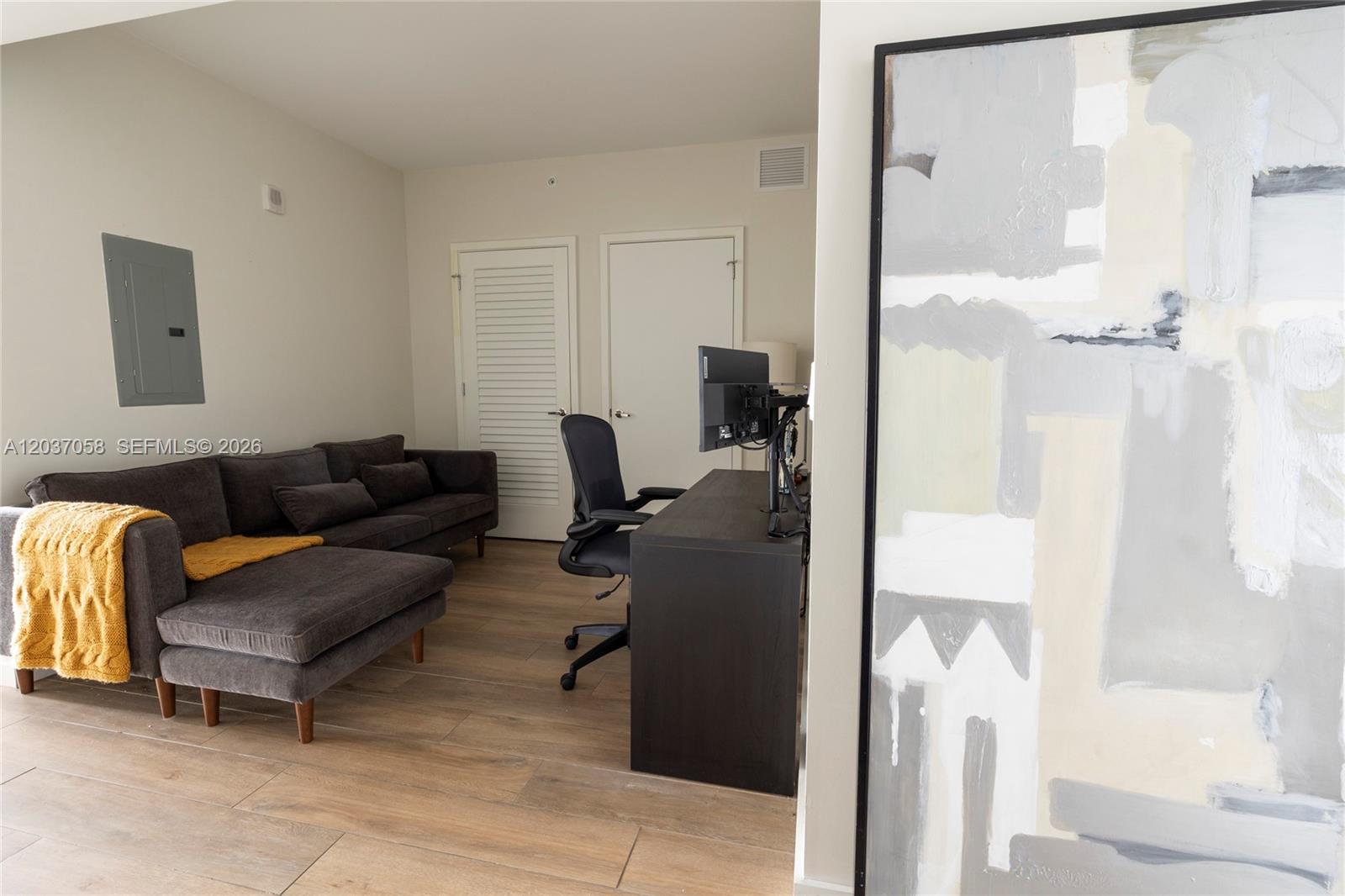 A room features a dark gray sectional sofa, a desk with a computer, and abstract art — 1010 Brickell Ave # 4311, Miami FL 33131, MIAMI, FL