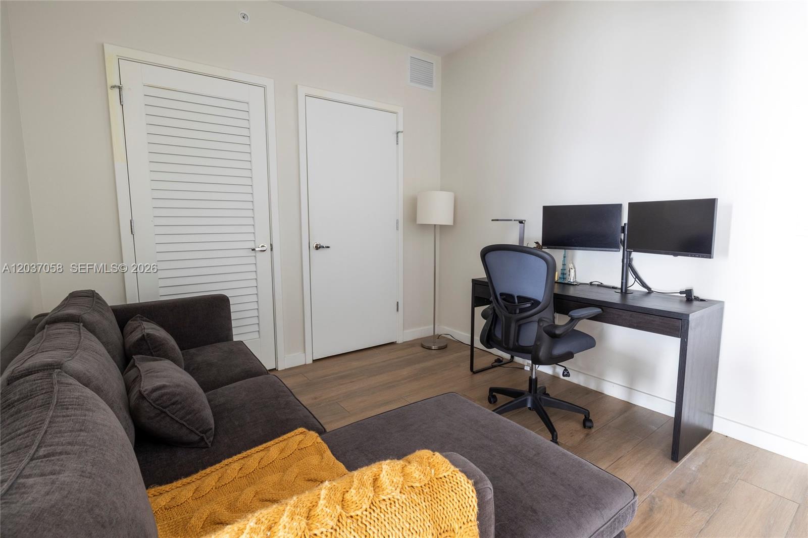 A room features a dark gray sofa with a yellow throw, a desk, and two doors — 1010 Brickell Ave # 4311, Miami FL 33131, MIAMI, FL