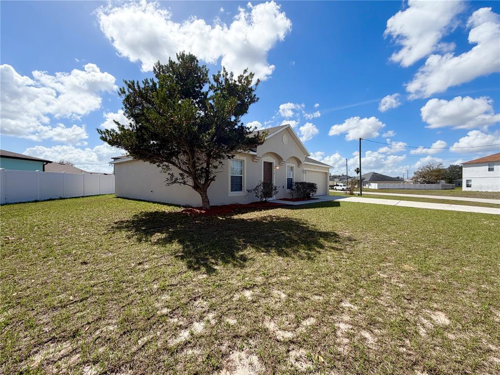 A single-story house with a beige exterior, a large tree, and a grassy front yard — 1914 MANATEE COURT, KISSIMMEE, FL