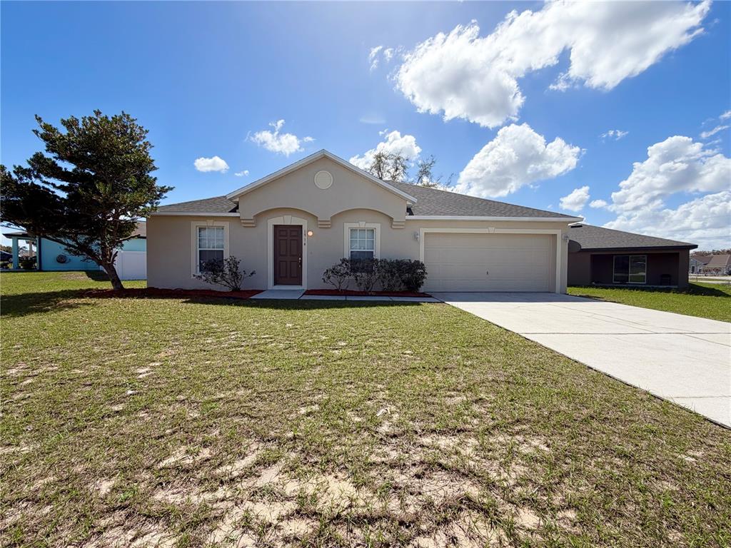 A single-story house with a beige stucco exterior, a two-car garage, and a front lawn — 1914 MANATEE COURT, KISSIMMEE, FL