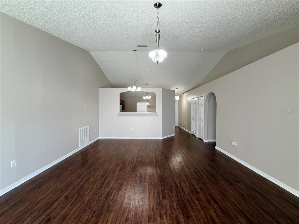 A living room with vaulted ceilings, dark wood-look flooring, and a kitchen pass-through window — 1914 MANATEE COURT, KISSIMMEE, FL