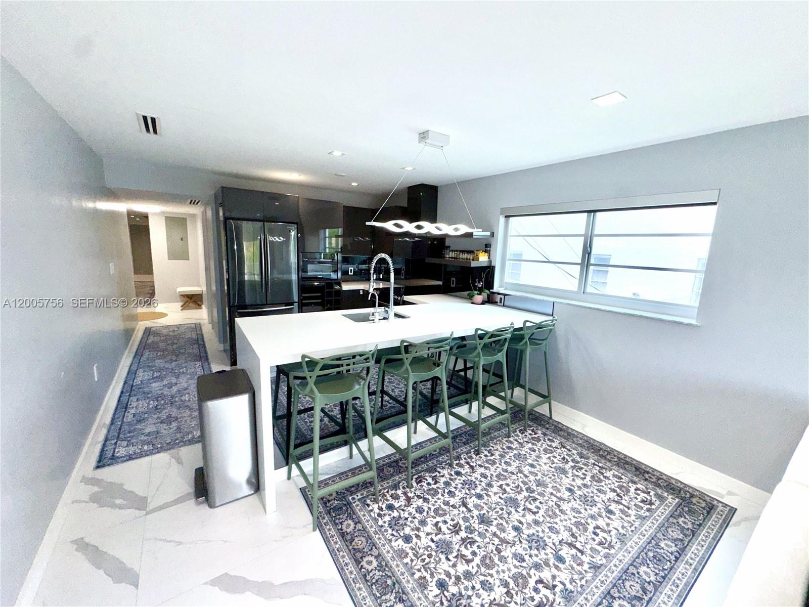 A modern kitchen features a white island with green stools and dark cabinetry — 1428 Euclid Ave # 207, Miami Beach FL 33139, MIAMI BEACH, FL