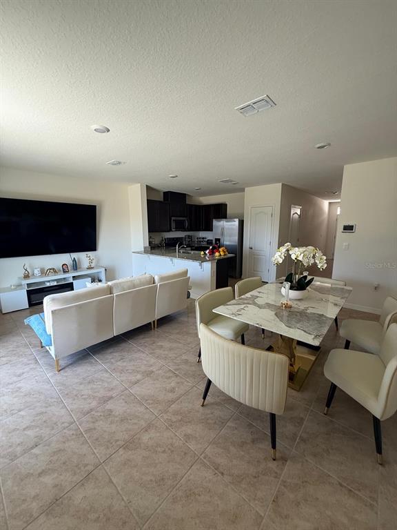 An open-concept living and dining area features tile flooring, a large television, and dark cabinetry — 1419 PLANK PLACE, DAVENPORT, FL