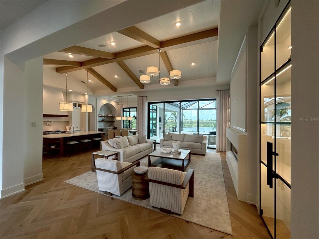 An open-concept living room features wood ceiling beams, herringbone floors, and a view of a pool — 258 CRYSTAL WATERS DRIVE, SARASOTA, FL