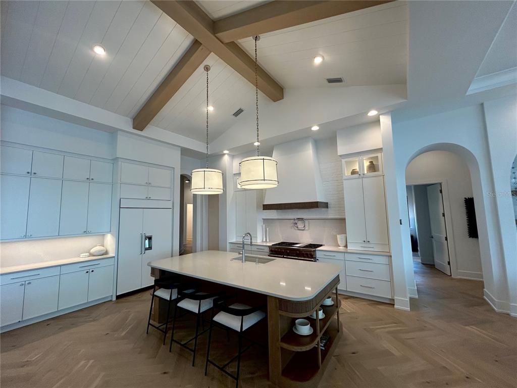 A kitchen features white cabinetry, a large island with seating, and a vaulted wood-beamed ceiling — 258 CRYSTAL WATERS DRIVE, SARASOTA, FL