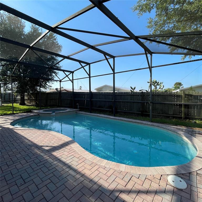 A screened-in swimming pool and spa with a brick paver deck and wooden fence — 845 BRIDGEFORD CROSSING BOULEVARD, DAVENPORT, FL